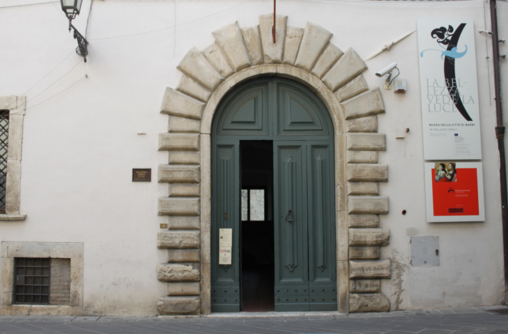 Stone portal of Palazzo Eroli in Narni, featuring a large arched door and museum information panels.