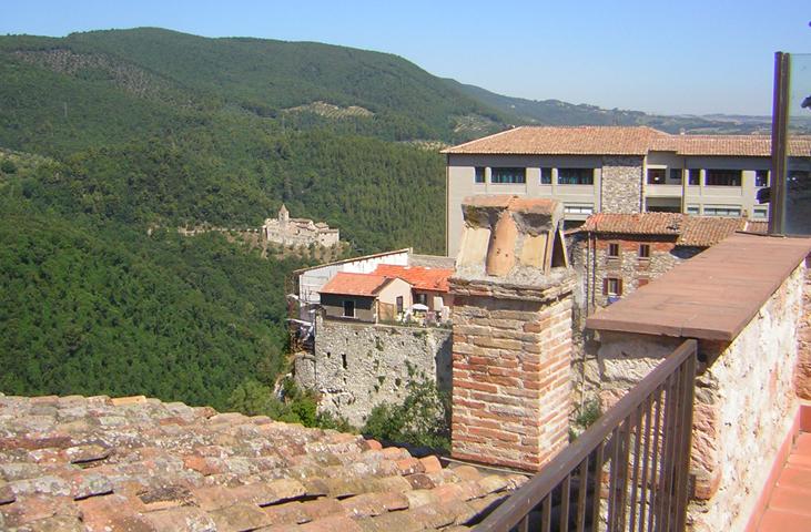 View from the rooftops of Narni towards wooded hills and San Cassiano Abbey, with chimneys and stone walls in the foreground.