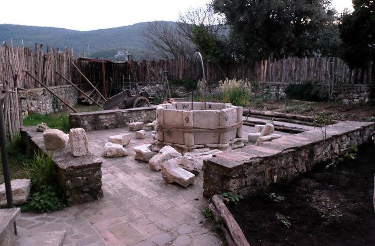 Octagonal stone well in an open courtyard surrounded by low walls and stone blocks, with hills in the background.